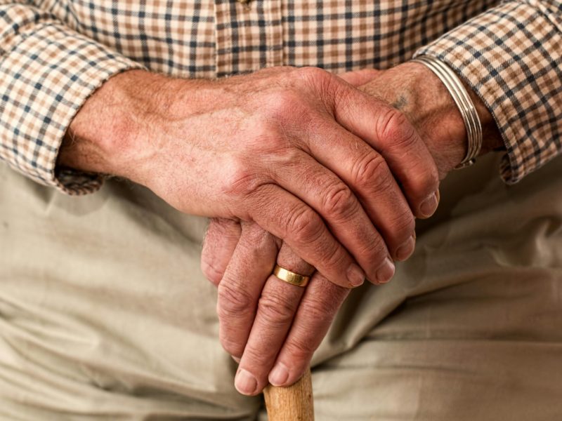A detailed image of elderly hands clasping a wooden cane, symbolizing aging and support.