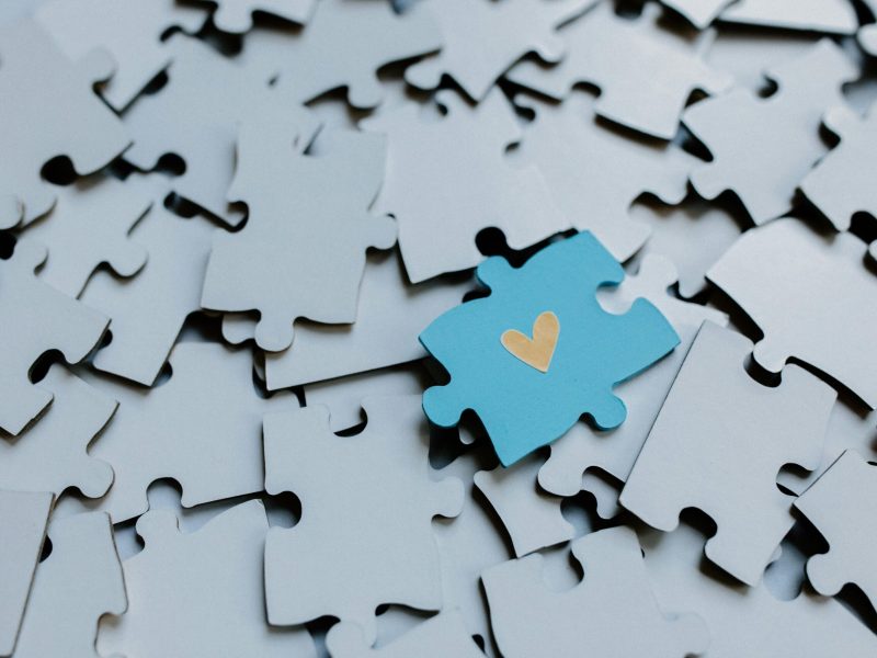 A single blue puzzle piece with a heart amid scattered pieces, symbolizing connection.